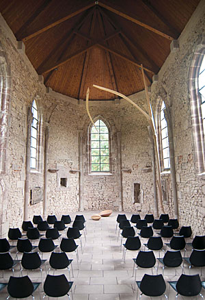 Weitwinkelansicht der Wintringer Kapelle mit leeren Stuhlreihen vor dem aktuellen Werk „In der Schwebe“