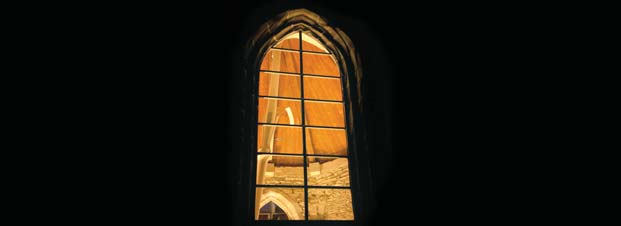 Blick aus der Dunkelheit durch ein Fenster in das erleuchtete Gewölbe der Wintringer Kapelle