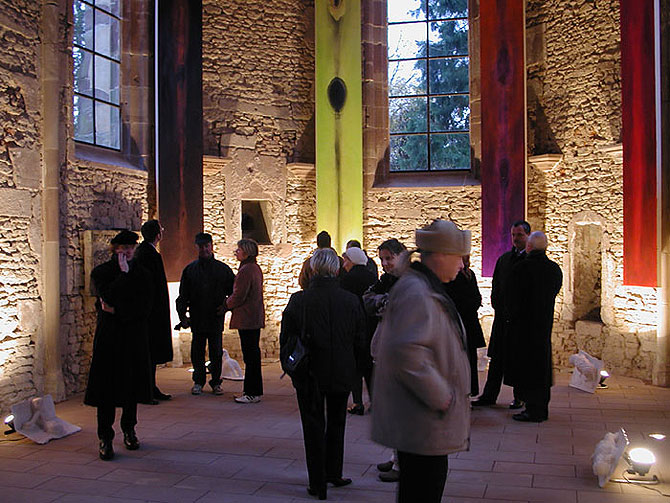 Ausstellungsbesucher betrachten im Inneren der Kapelle angestrahlte Kunstwerke an den Wänden